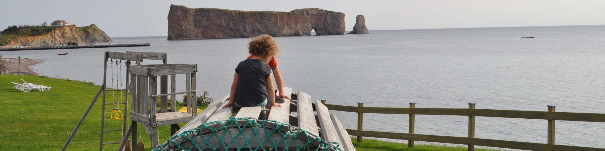 Children playing on an outdoor playground, view of the sea and Percé Rock